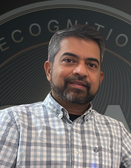 A man wearing a plaid shirt poses in front of the Global Recognition Awards logo